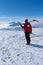 Ski patroller on snow caped mountain is walking against sun with a red rescue jacket and a shovel on his shoulders