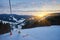 Ski resort in beautiful sunset light. View from the top: ski tracks, pine tree forest and mountains in the background