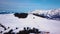 Ski resort in sunny weather. Snow on the ski slope of a wooded mountain. Many tourists near the ski lift station and cafe. Aerial