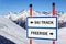 Ski track and freeride delimitation sign with arrows showing opposite directions against snowy mountain  blue sky winter