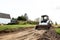 A skid steer loader clears the site for construction. Land work by the territory improvement. Machine for work in confined areas.