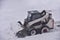 Skid-steer loader during snow removal on the road after a snowfall. Snow clearing is the job of removing snow after a snowfall to