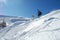 Skier in action on a sunny winter day.  High jump from the hill followed by snow powder. Blue sky and white snowy mountains on bac