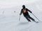 Skier in black downhill skiing on a ski slope. View from back