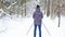 Skier in hat with pompom with ski poles in his hands with in snowy forest with snow. Cross-country skiing in winter forest, outdoo