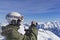 Skier man with orange ski glasses in white helmet make photoshoot on top in Alps mountains. On the background of