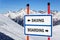 Skiing and snowboarding bifurcation sign with arrows showing opposite directions against snowy mountain  blue sky winter