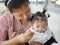 Skilled Asian mother using small spoon to feed her baby girl, 12 months old, at a cafeteria