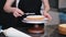 Skilled female confectioner smearing organic cake layers with knife standing at table