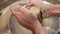 Skilled potter turns clay on potter's wheel and gives it elongated shape. Closeup of hands, side view. Concept of making