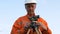 Skilled surveyor in orange jumpsuit and helmet at theodolite