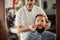 Skillful male barber is serving his client