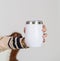 Skillfully composed mockup showcasing a woman elegantly holding a white blank tumbler, striking a simple pose at an indoor studio