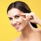 Skin care beauty. Ðappy smiling woman pointing, touching skin, applying cream. yellow background.