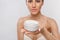 Skin care. Beauty Concept. Young woman holding cosmetic moisturizing cream. Soft skin and naked shoulders, model with light nude m