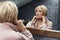 Skincare Routine. Mature Woman Touches Face Skin In Front Of The Mirror Reflection.