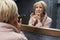 Skincare Routine. Mature Woman Touches Face Skin In Front Of The Mirror Reflection.