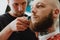 Skinhead bearded tattooed man in barbershop. Barber cuts hair wi