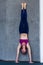 Skinny barefoot woman in sportswear doing handstand against the wall indoors