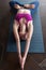 Skinny girl in sports bra doing core stretching exercise with back bend and legs in lotus pose lying on mat at home