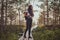 Skinny woman is hiking by the wooden path in the middle of lush pine forest.