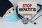 Skull in mask and cap, stethoscope and easel with canvas on which it is written - STOP HEPATITIS