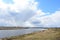 Sky, clouds. Meandering river. Grass on the low banks of the river. In the distance, the forest and the village. Rural view