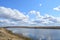 Sky, clouds. Meandering river. Green grass on the low banks of the river. Forest in the distance. Rural view