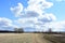 Sky, clouds. Road along the field. Forest and trees in the distance. Rural view of nature