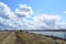 Sky, clouds. Rural road. River. Boundless field. Forest in the distance. Rural view of nature