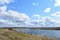 Sky, clouds. Wind. Meandering river. Grass on the low banks of the river. Forest in the distance. Rural view