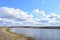 The sky is covered with clouds. Meandering river. Green grass on the low banks of the river. In the distance, a forest, a village