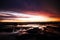 Sky with deep hanging storm clouds and wet sludge during low tide swathed in yellow and red bright light during sunset