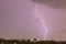 Sky with lightning striking hills behind small town