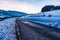 Sky reflection on empty, destroyed cracked asphalt road in winter. Big snow around and snow-covered mountains at sunset. Austria