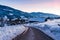 Sky reflection on empty destroyed cracked asphalt road in winter. Big snow around and snow-covered mountains at sunset. Austria