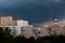 The sky is very dark blue over multi-storey buildings before a thunderstorm, with pipes visible on the horizon