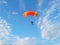 A skydiver with a bright orange parachute flies against a blue sky