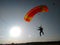 A skydiver with a bright orange sports parachute wing flies before landing