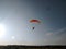 A skydiver with a bright orange sports parachute wing flies before landing
