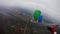 Skydivers with colorful parachutes fly over green field in cloudy sky. Extreme