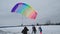Skydivers with multi-colored parachutes land on a background of cloudy sky and snow