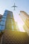 Skyscraper facades on a bright sunny day with sunbeams in the blue sky and passenger jet plane flying on above