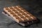 A slab of milk chocolate on top of a slab of dark chocolate  on black slate. Space for text. Blurred background