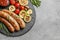 Slate plate with delicious barbecued sausages and vegetables on gray background.