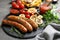 Slate plate with delicious sausages and vegetables served for barbecue party