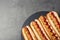 Slate plate with hot dogs on grey background, top view.