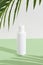 A sleek bottle of cosmetic cream casts captivating shadows on a lush green backdrop in minimalist style