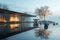 A sleek, cubist house by a still, reflective lake at dawn. The cool morning light reveals an Easter-themed sculpture garden