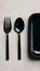 Sleek, minimalist trio black fork, spoon, rectangular tray on neutral background